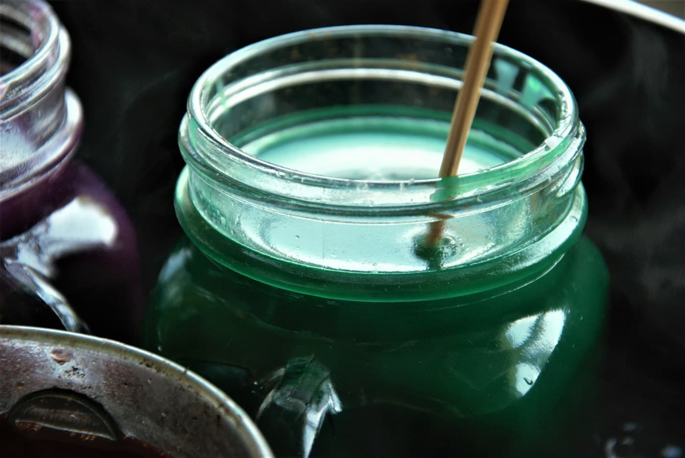 Green wax melting in a glass jar with a stirring stick